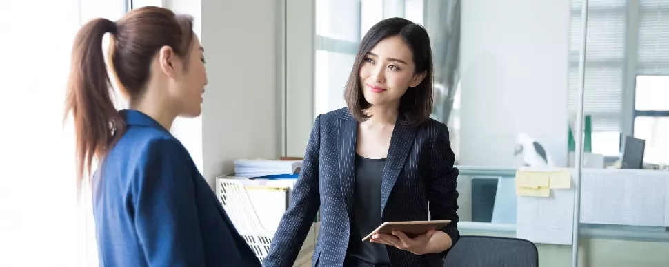 Two people in formal attire having a conversation in an office.