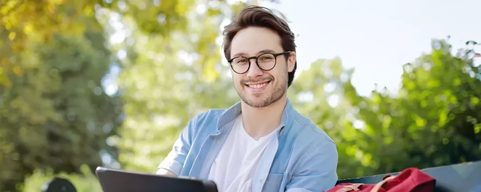 Person smiling outdoors sitting on a bench with a tablet.