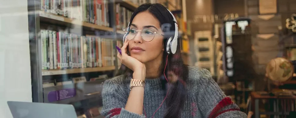 Person wearing headphones sitting in a library, looking thoughtful.