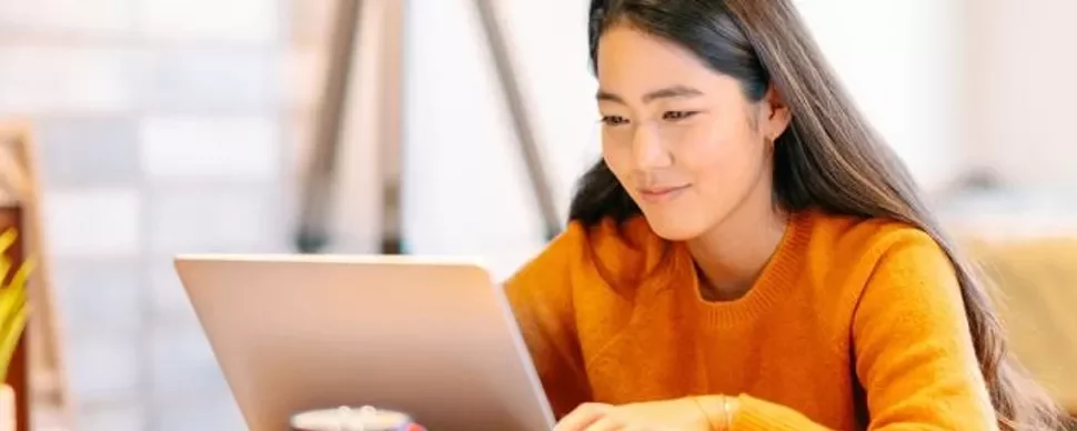 Person in orange sweater working on a laptop at home.