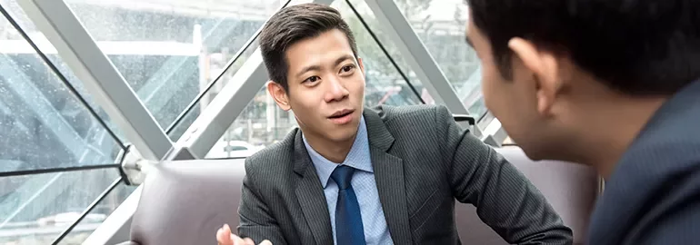 Two people in business attire are engaged in a conversation in an office setting.