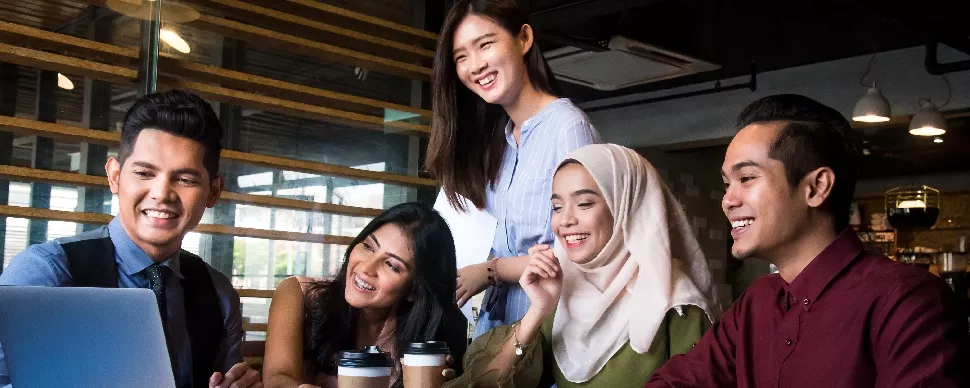 Group of people smiling and discussing around a laptop in a modern office.