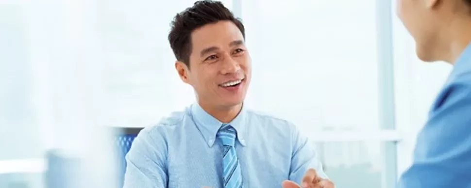 Person in a blue shirt smiling and talking to someone in a light office.