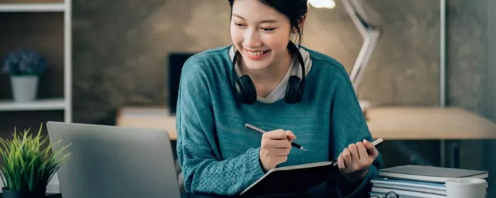 Person with headphones studying on a laptop at a cozy desk.