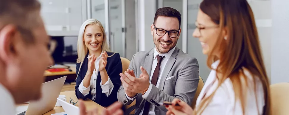 Group of professionals in a meeting, smiling and clapping.
