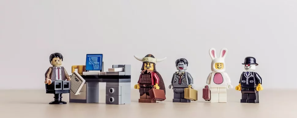 Assorted LEGO figures standing in line next to a desk with a computer.