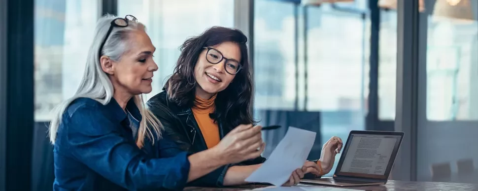 Two women of different age groups and ethnicities looking through a document together