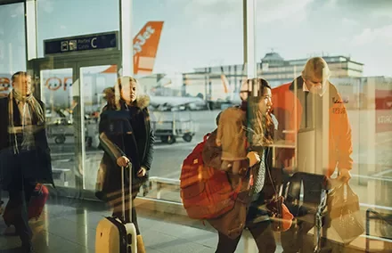 Travelers with luggage walk through a bright airport terminal.