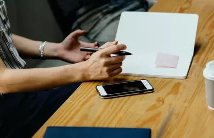 Person holding a pen over an open notebook with a pink sticky note.