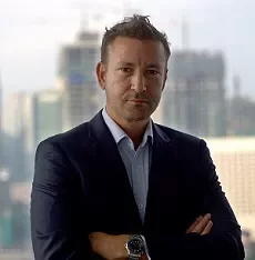 Person in a suit standing with arms crossed, cityscape in background.