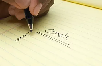Handwriting goals on a yellow notepad.