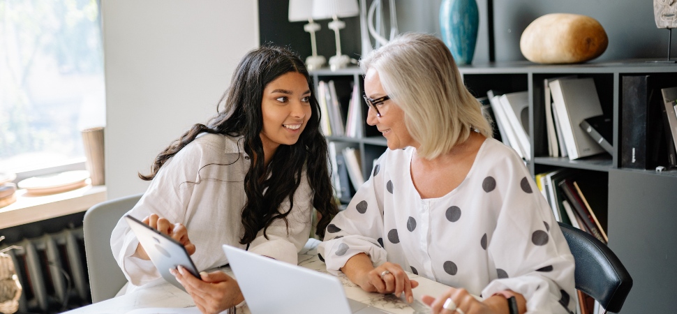 A younger office worker chatting with an older female colleague in an office setting